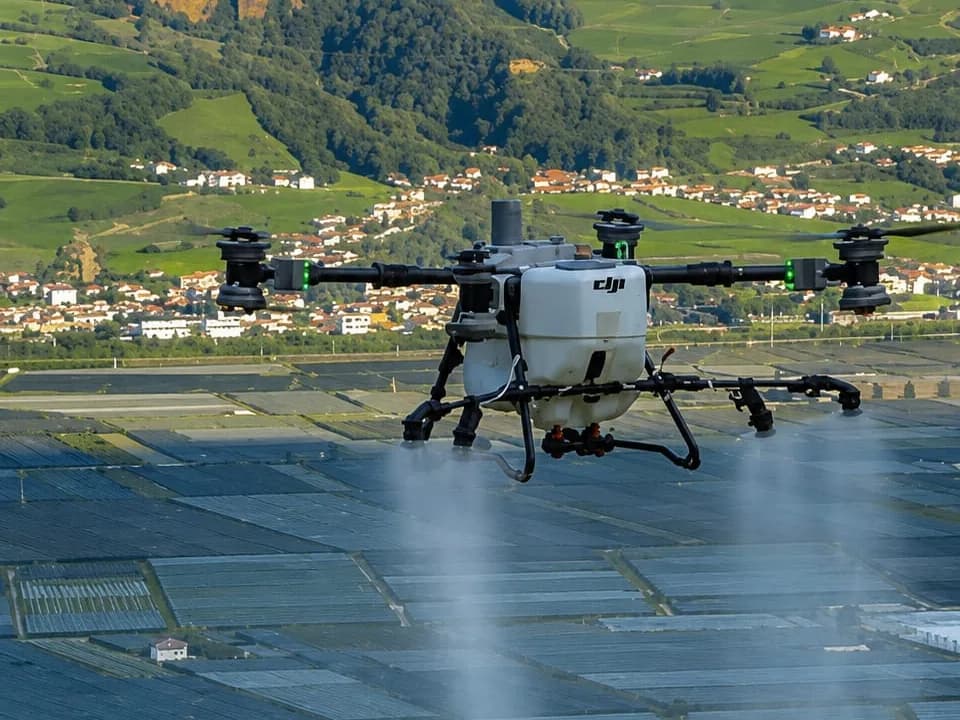 Sprühdrohne im Flug über einer Kulturlandschaft, unter den Düsen steht der Sprühnebel