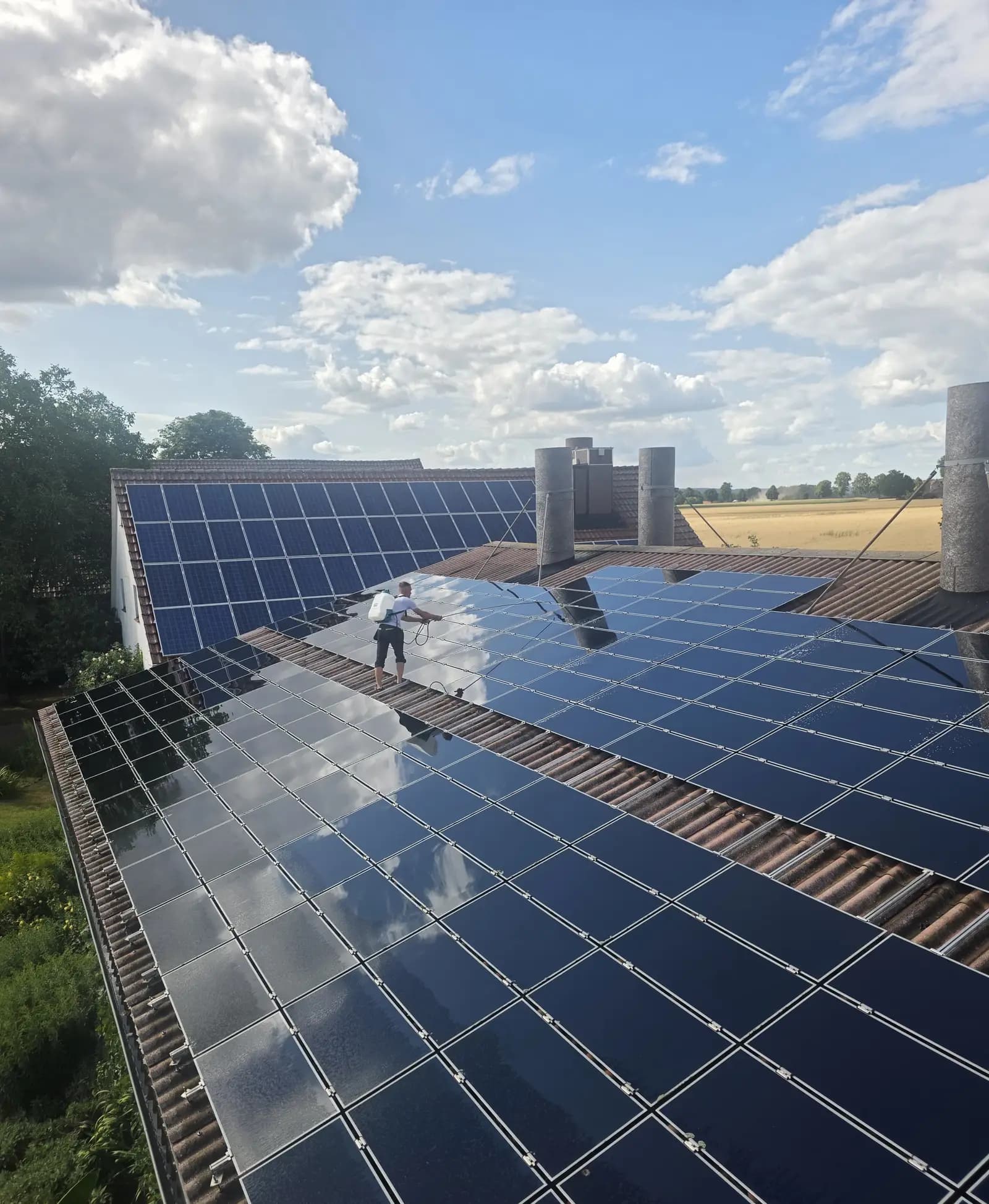 Große Photovoltaikanlage auf einem Hofdach, ein Mitarbeiter reinigt die Modulreihen mit der Lanze