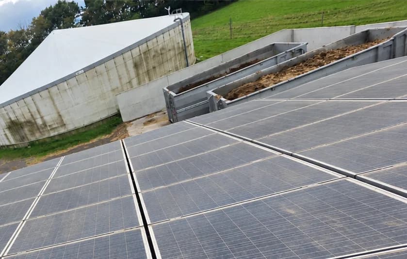 Photovoltaikanlage auf einem Hallendach neben Fahrsilo und Biogasbehälter, Module vor der Reinigung matt und grau belegt