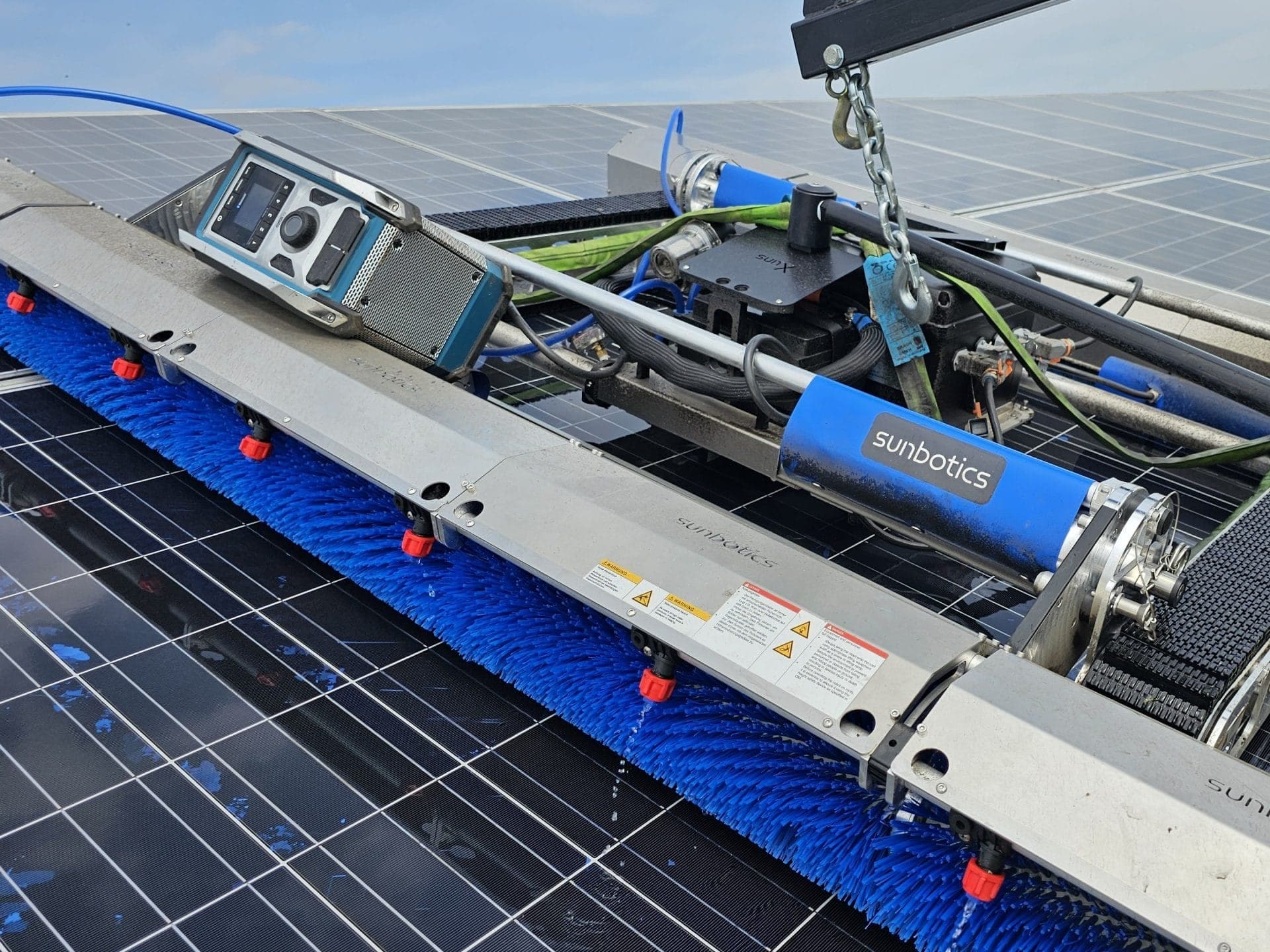 Waschroboter mit blauer Bürstenwalze auf nassen Photovoltaikmodulen
